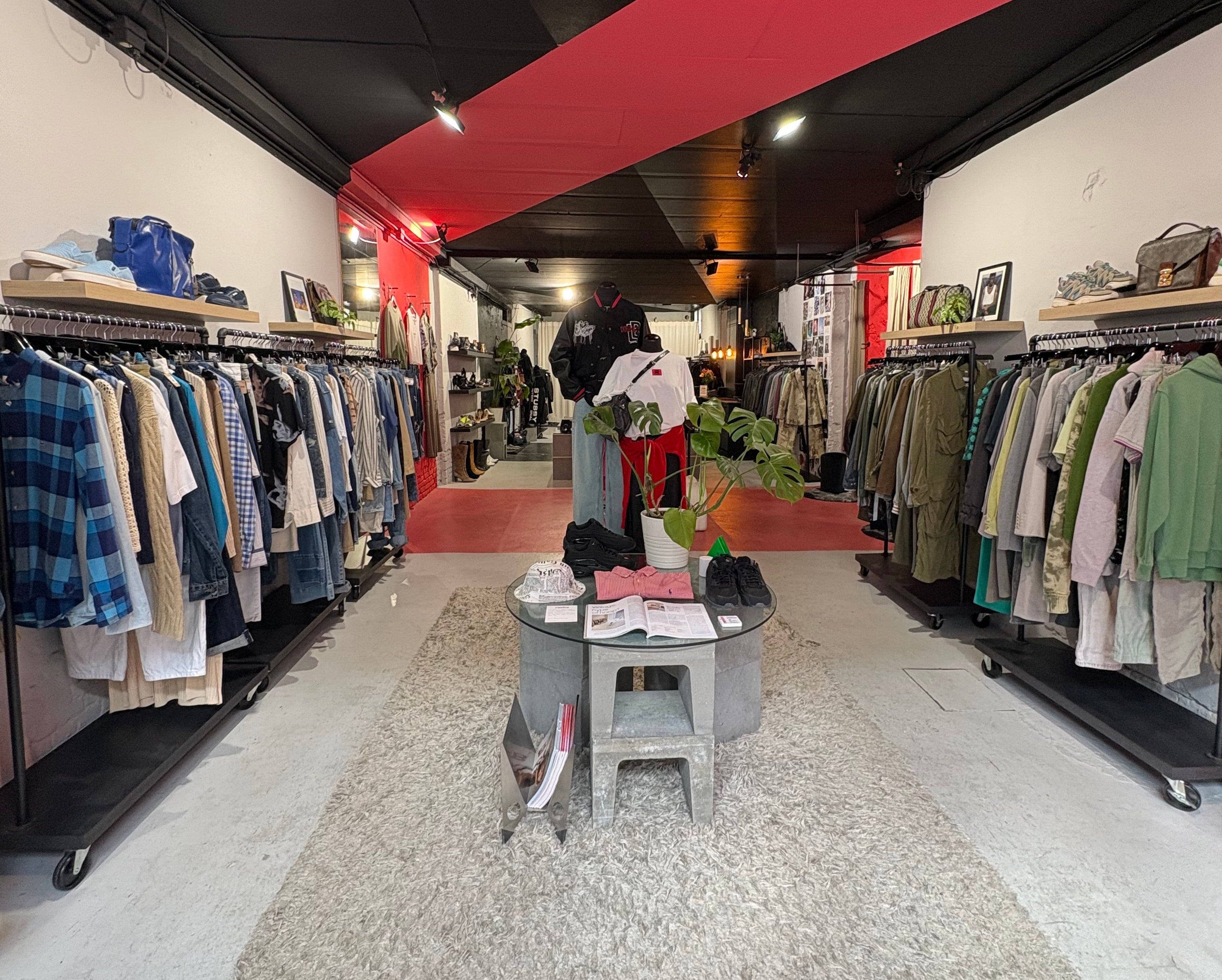 Clothing store interior with racks of clothes and a red wall.